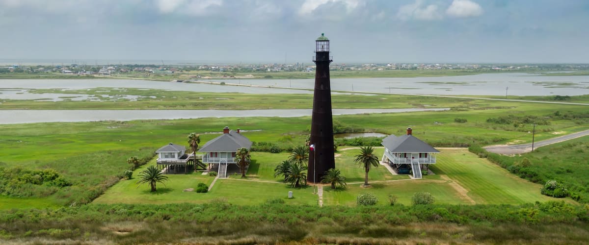A lighthouse, two houses, and a marshy landscape.