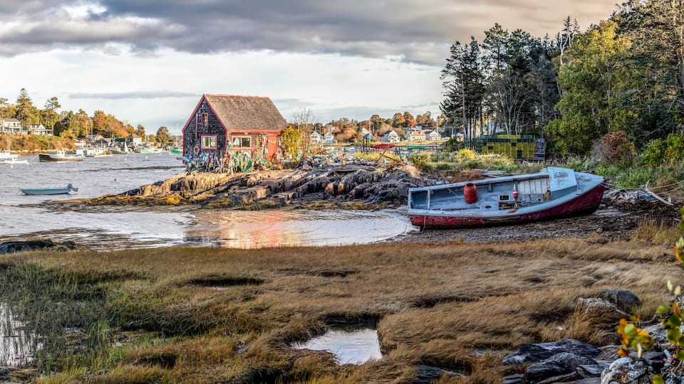 A coastal scene with a house, boats, and a rocky shoreline.