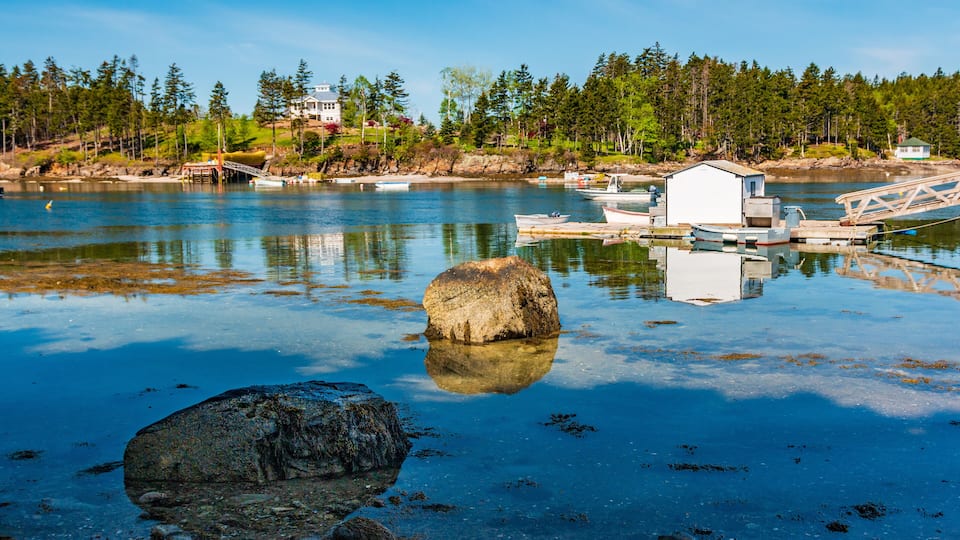 A calm lake with a dock, a large rock in the foreground, and houses in the background.