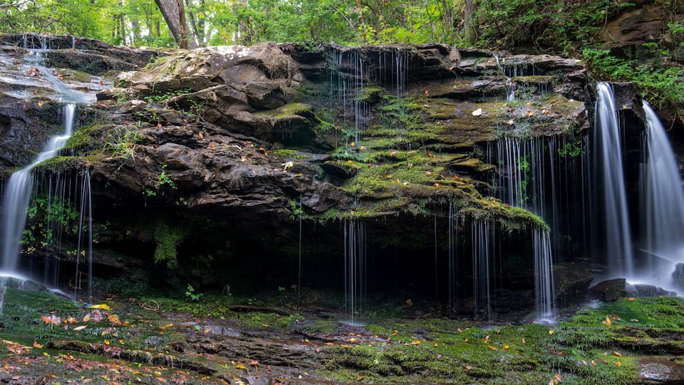 A multi-tiered waterfall surrounded by moss-covered rocks and autumn leaves.