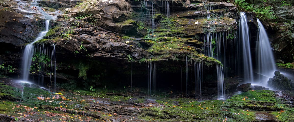 A multi-tiered waterfall surrounded by moss-covered rocks and autumn leaves.