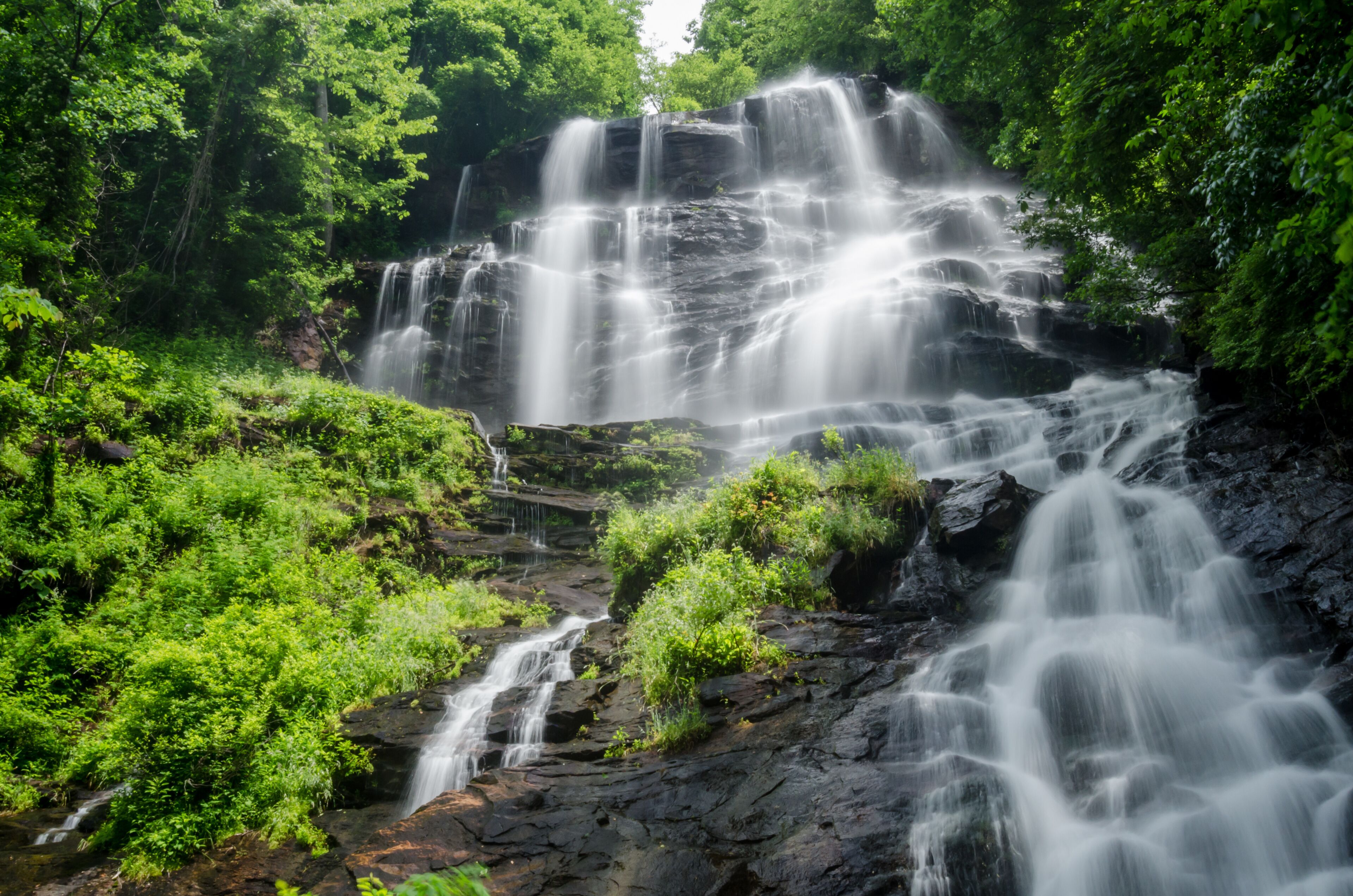 A multi-tiered waterfall surrounded by lush greenery.