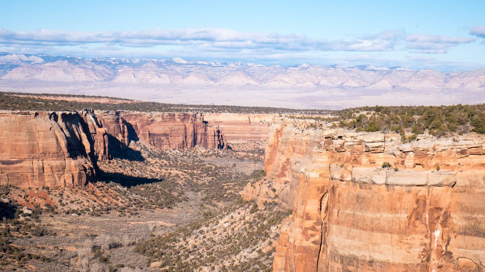 A canyon with layered rock formations and sparse vegetation.
