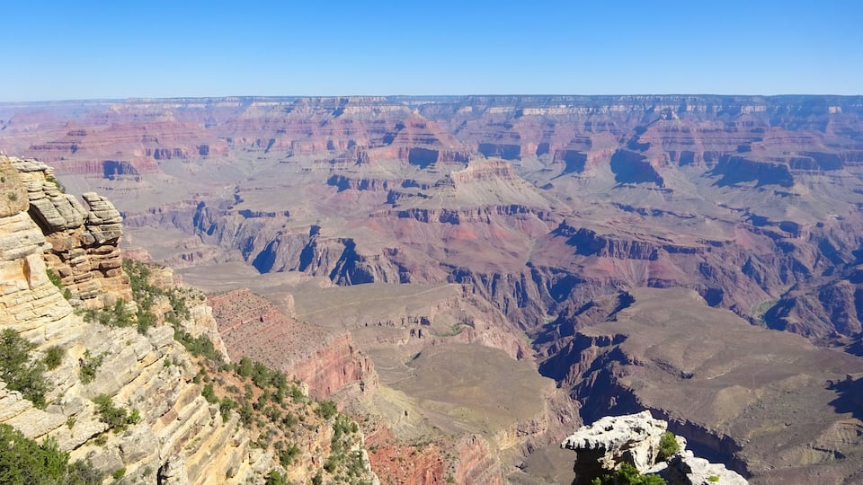 A vast canyon with layered rock formations and sparse vegetation.