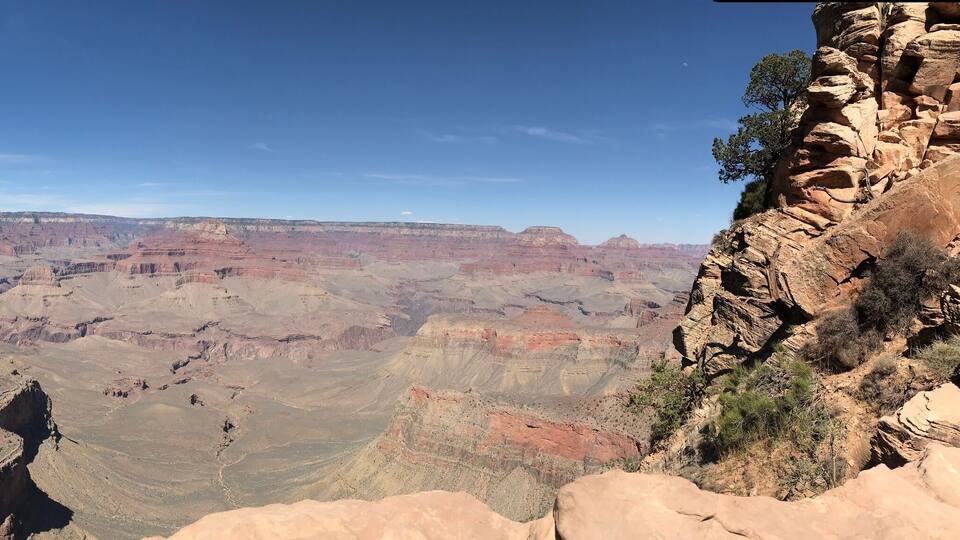 A vast canyon with layered rock formations and a clear blue sky.
