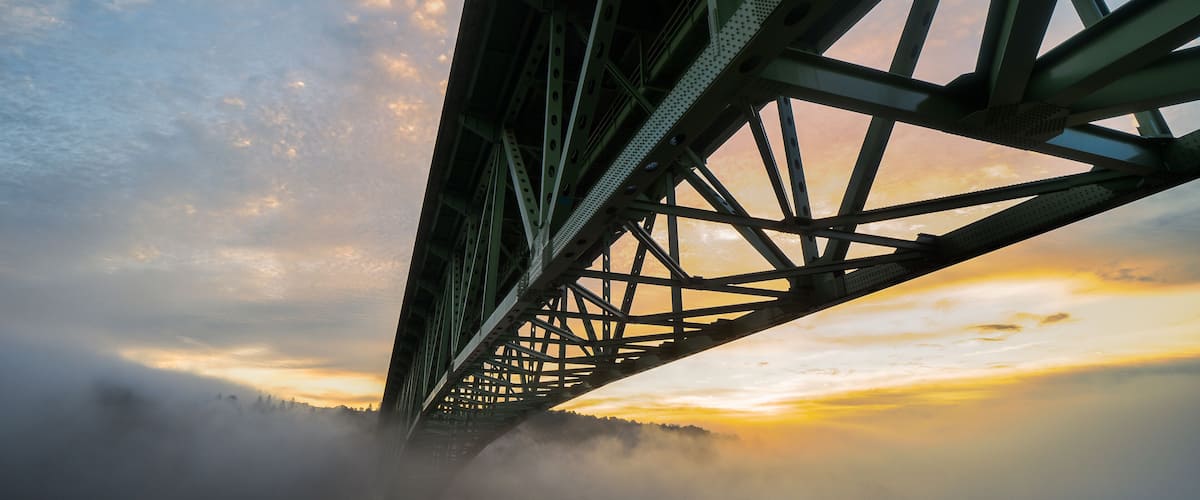 A bridge with a steel structure and a misty landscape below.