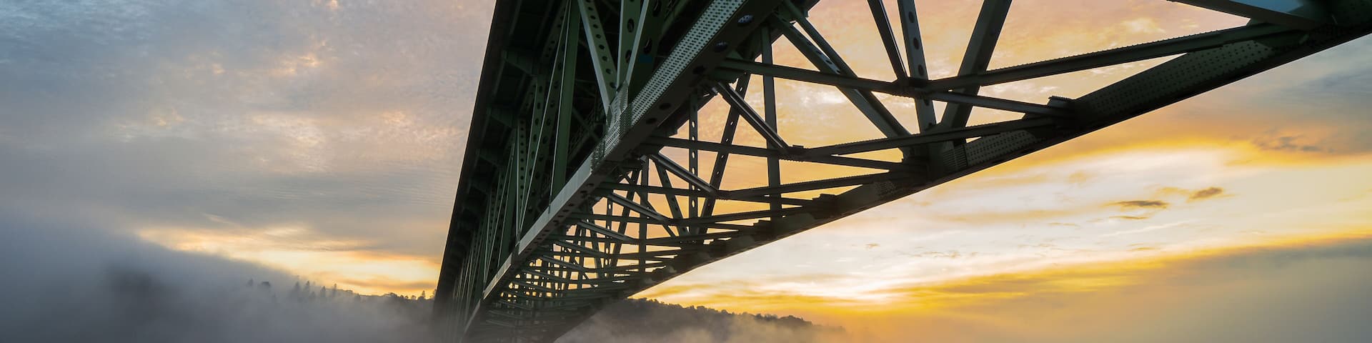 A bridge with a steel structure and a misty landscape below.