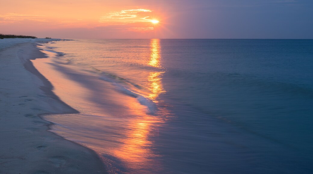 Ein Strand bei Sonnenuntergang, das ruhige Meer spiegelt die Farben des Himmels.