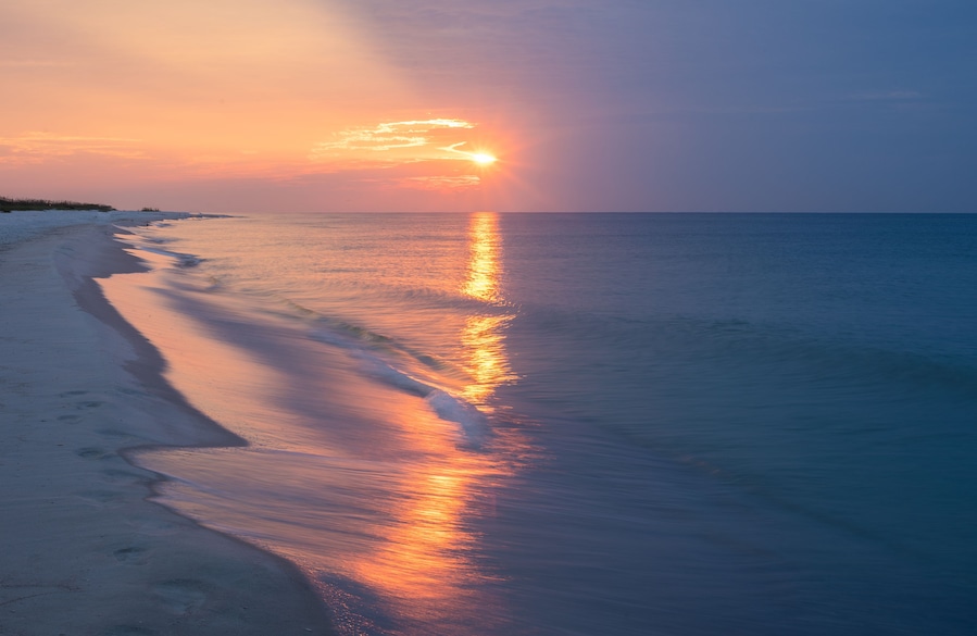 Una playa al atardecer con un mar tranquilo reflejando los colores del cielo.