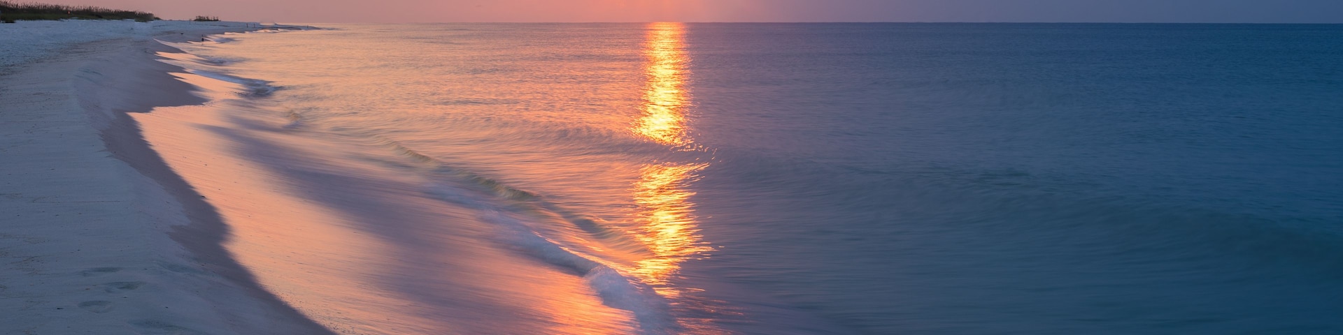 Una playa al atardecer con un mar tranquilo reflejando los colores del cielo.