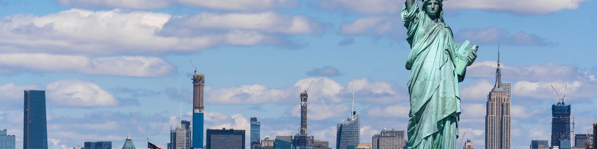 The Statue of Liberty in New York City with a view of the skyline and a ferry in the water.