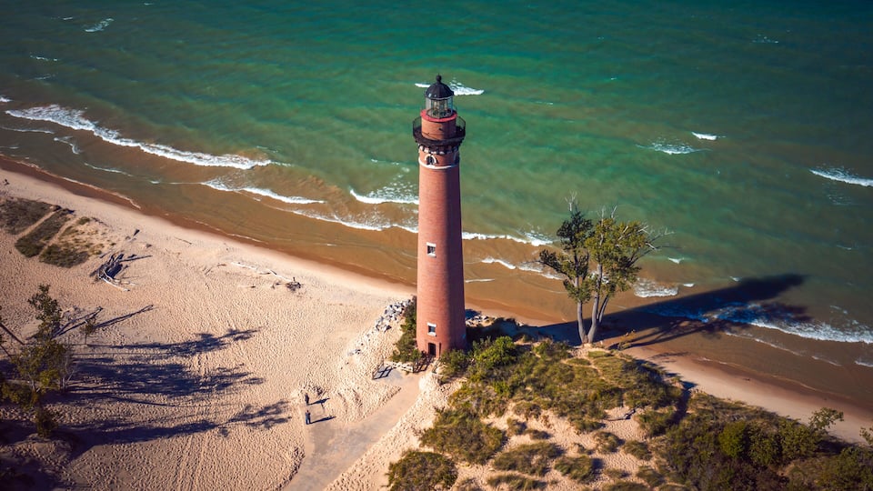 A lighthouse on a sandy beach with clear blue water.
