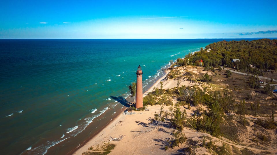 A coastal landscape with a lighthouse, beach, and forested area.