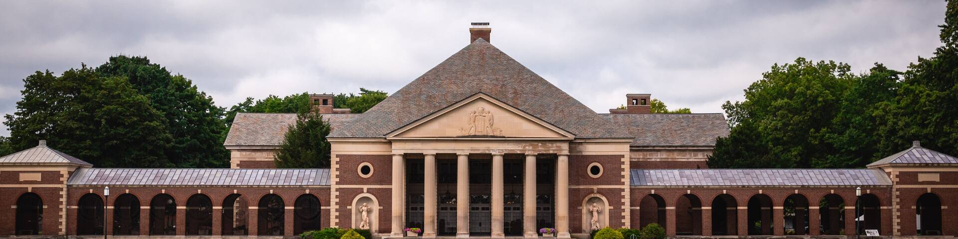 A large brick building with a central pediment and columns, surrounded by a well-maintained lawn and a reflecting pool.
