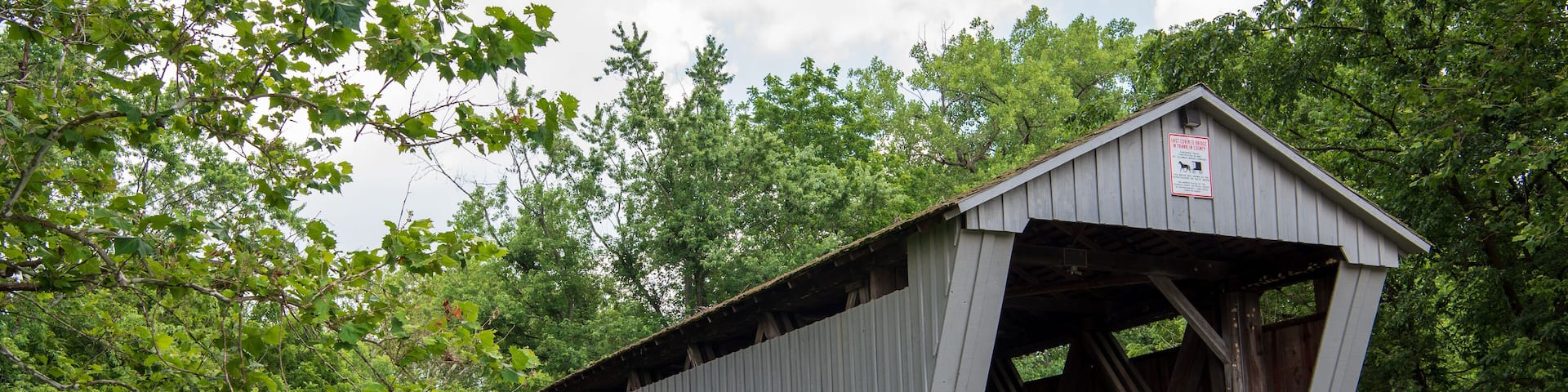 A covered bridge with a sign, surrounded by lush greenery and a small stream.