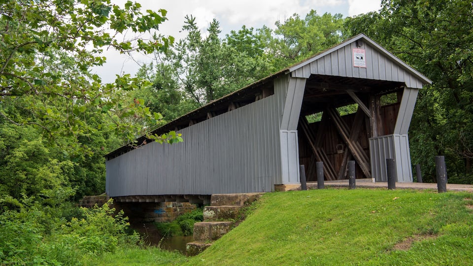 A covered bridge with a sign, surrounded by lush greenery and a small stream.