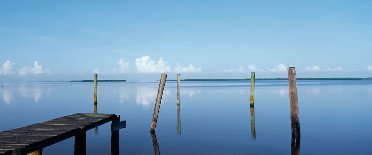 A wooden pier extending into calm water with a clear sky and distant land.