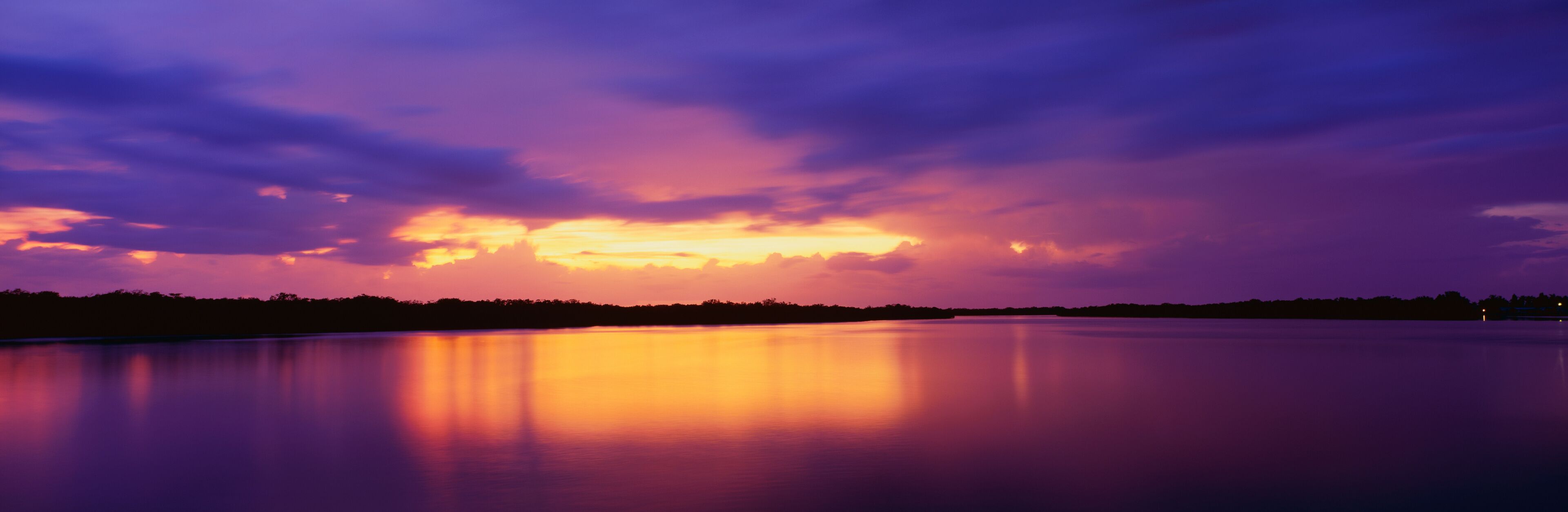This is the ocean and Pine Island at sunset. There is a pinkish purple cast in the sky that is reflected in the water. The nearby land is in silhouette.