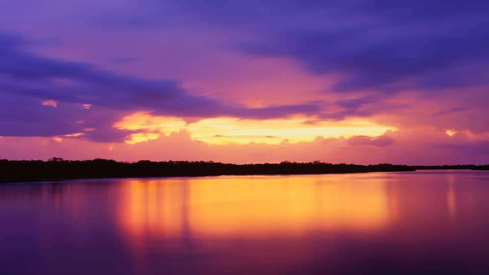A calm lake reflecting a sunset sky with purple and orange hues.