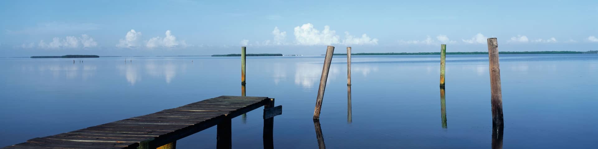 This is the morning view of Pine Island Sound. Its pier juts out from the left side with wooden pylons standing up out of the water near the shore.