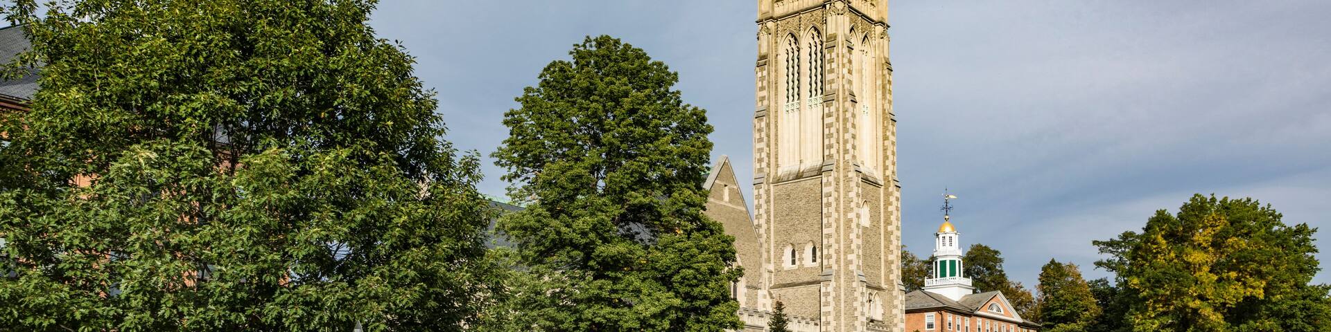 A historic building with a tall tower, surrounded by lush green trees and a well-maintained lawn.