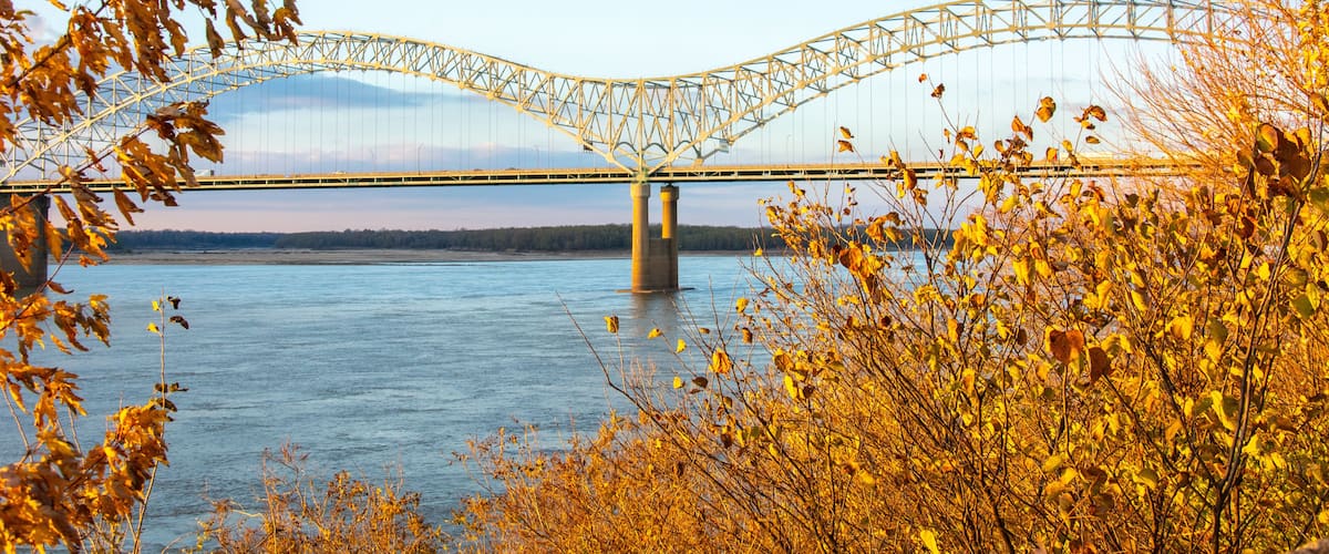 The tied-arch Hernando de Soto Bridge carrying Interstate 40 across the Mississippi River between West Memphis, Arkansas, and Memphis, Tennessee as seen from Mud Island Park on sunset with fall colors