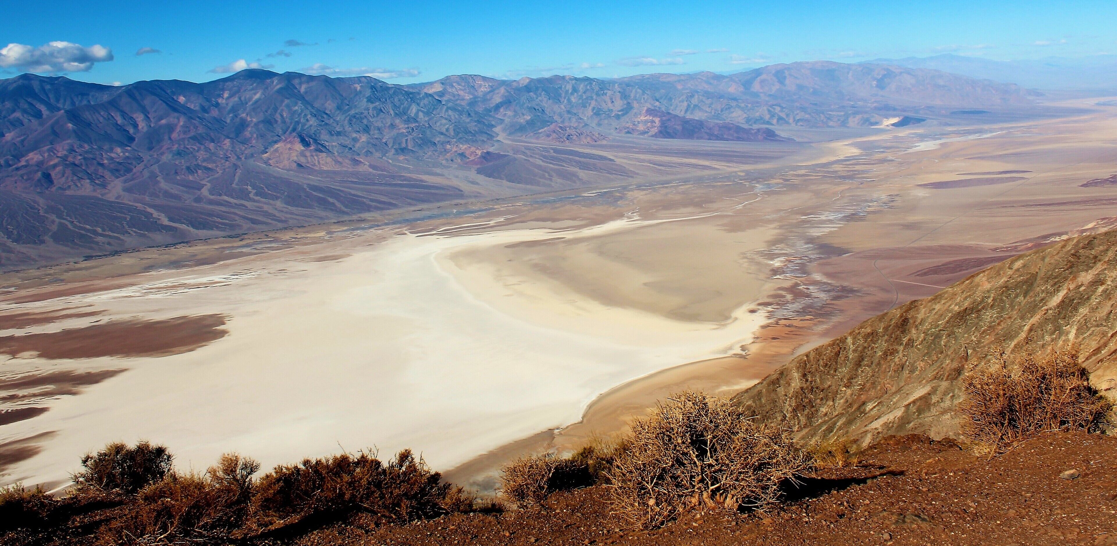 I took this photo at Death Valley National Park, in California USA. From Dante's View! One of the best viewpoints in this otherworldly national park. I had a memorable time there in December 2016. My 1st time ever in California. But it was only for 1 day, as I was based in Las Vegas. But Death Valley National Park was somewhere I've wanted to go for a very long time. I love this kind of foreboding and otherworldly landscape! And more about this photo and Dante's View: It's a viewpoint terrace at 1,669 m (5,476 ft) height, on the north side of Coffin Peak, along the crest of the Black Mountains, overlooking Death Valley. All quite dark and macabre names, if I do say so myself! Dante's View was even used as a filming location in the 1st Star Wars film. And that big white spot in this photo is a huge salt flat at Badwater Basin. Badwater Basin is the the lowest point in North America, at 282 ft (86 m) below sea level. And Death Valley itself is notoriously hot in many months of the year. It's one of the hottest places in the world in the summertime. I'm glad I went in a December ;). But from this viewpoint it was so cold from the chilly temperature and strong wind that I was forced to quickly put on gloves and a hat ;). All part of the incredible experience! 