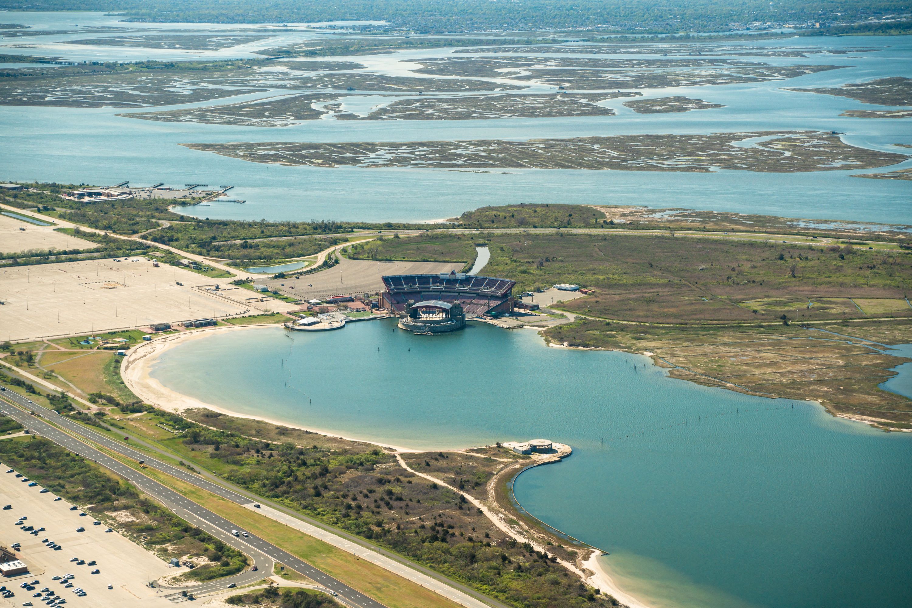 An aerial view of a coastal area with a large stadium, a marina, and a highway.
