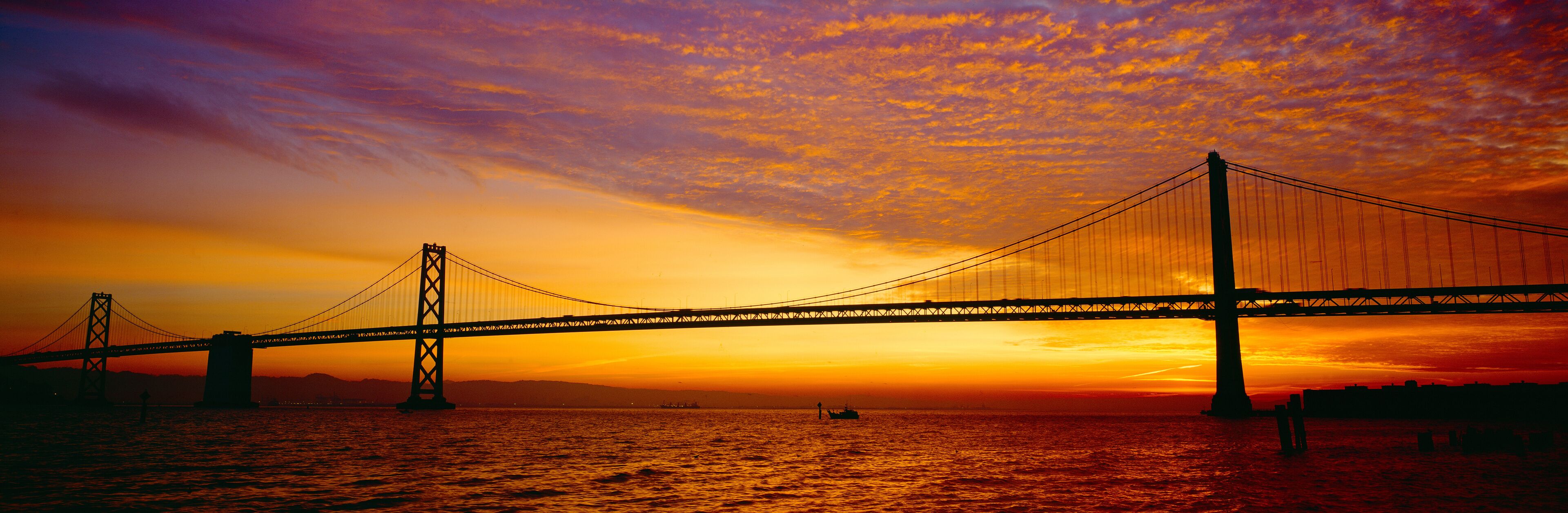 A suspension bridge at sunset with a vibrant sky.