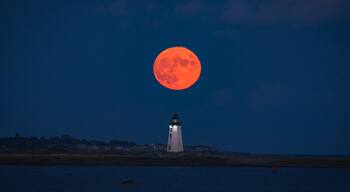 A lighthouse at night with a full moon in the sky.