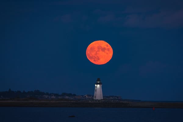 A lighthouse at night with a full moon in the sky.