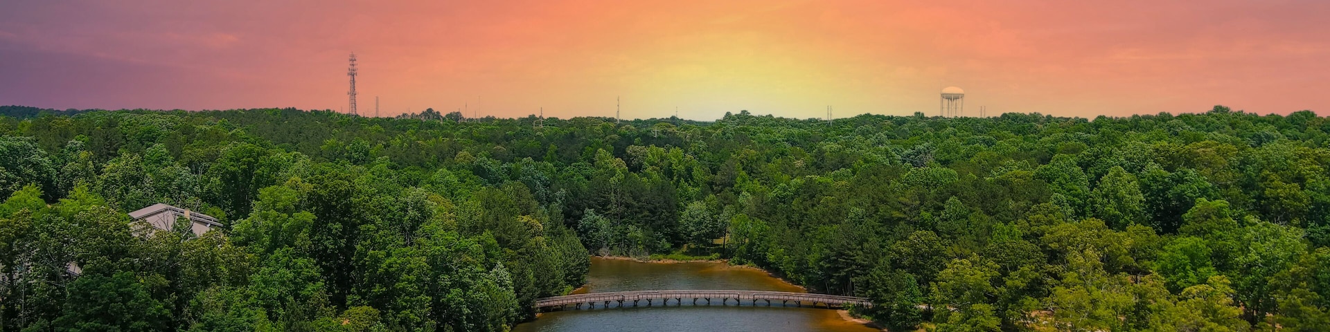 Um rio com uma ponte, cercado por uma floresta verde densa, sob um céu ao pôr do sol.
