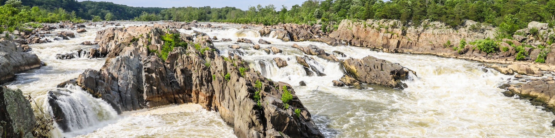 A river with multiple rapids and waterfalls, surrounded by rocky terrain and dense greenery.