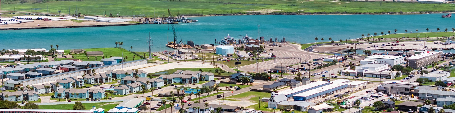 Une zone industrielle comprenant un port de plaisance, des conteneurs de transport et une vaste étendue d’eau.