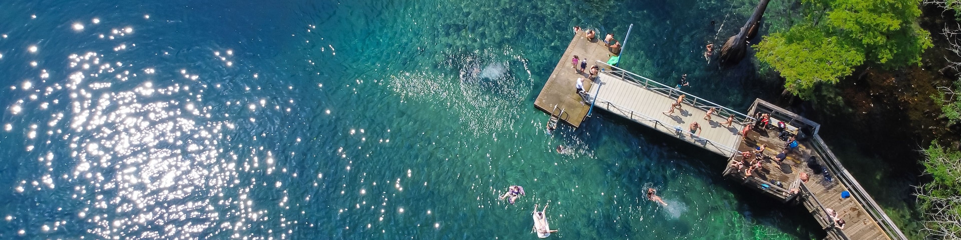A pier extending into a clear blue body of water with people swimming and sunbathing.
