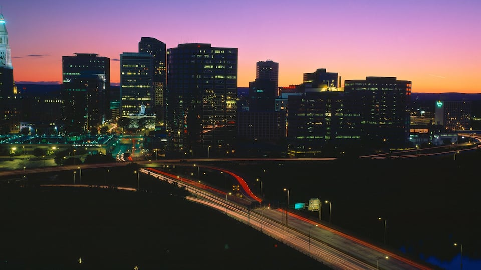 A city skyline at dusk with illuminated buildings and a prominent tower.