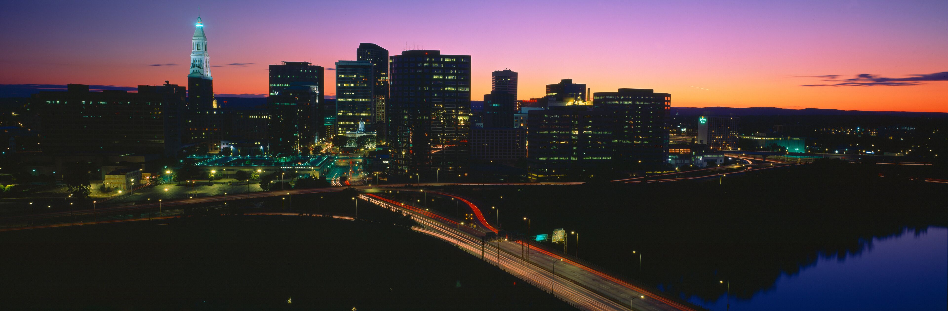 A city skyline at dusk with illuminated buildings and a prominent tower.