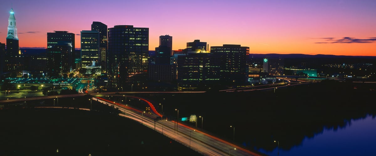 A city skyline at dusk with illuminated buildings and a prominent tower.