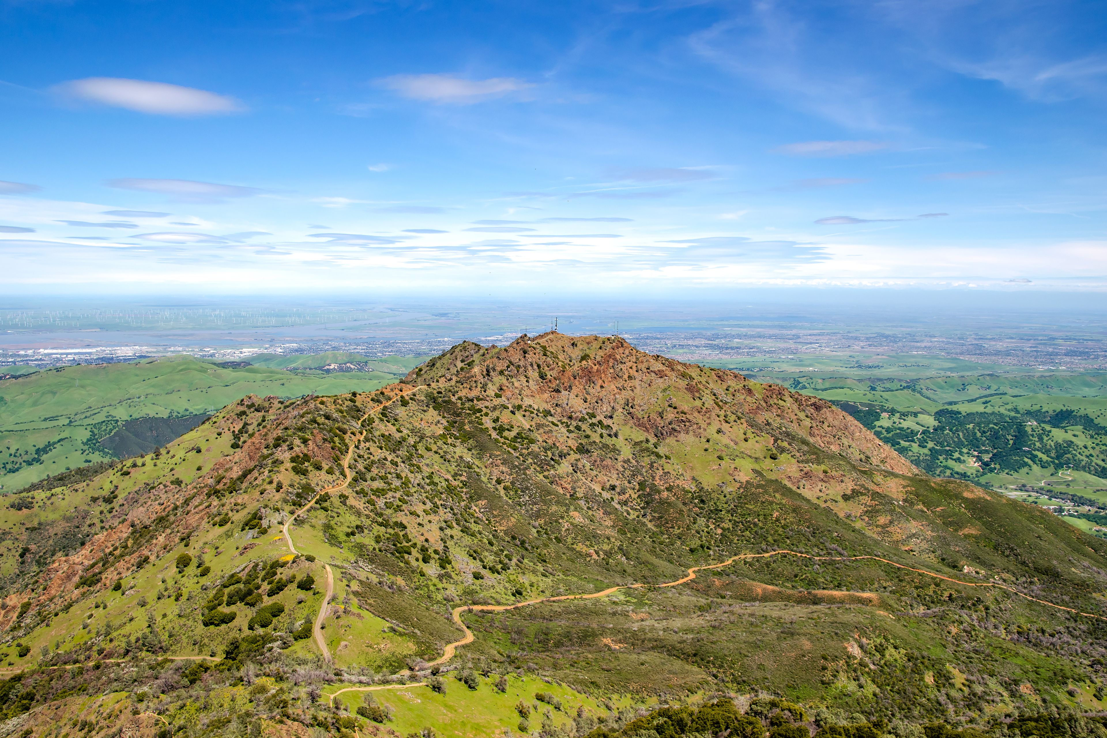 A mountain with a winding path and a city in the distance.