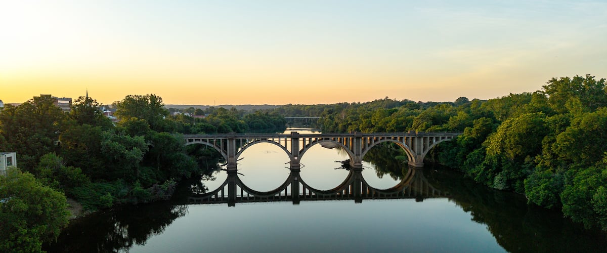 A bridge over a calm river with trees on both sides, reflecting the structure.