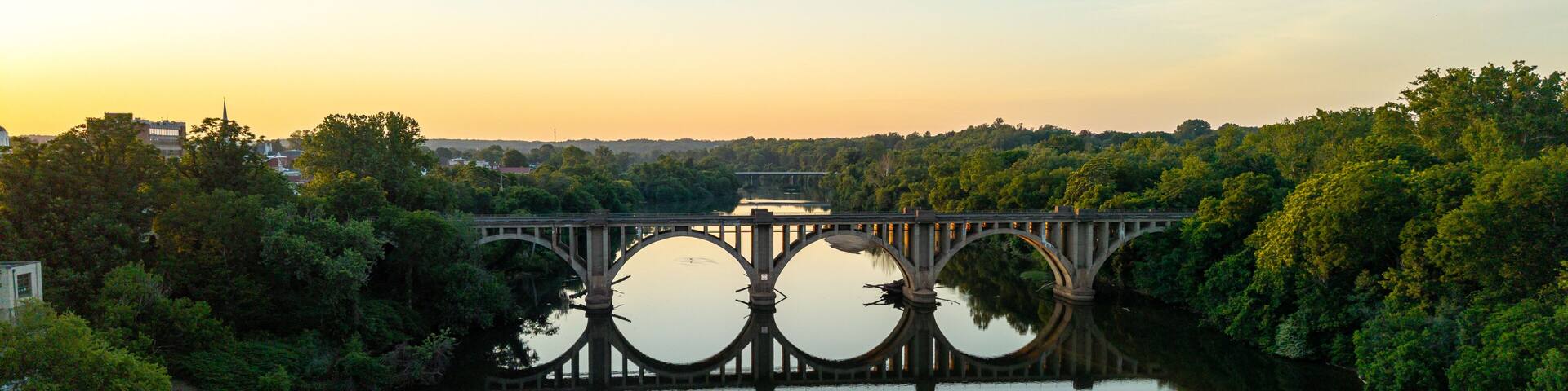 A bridge over a calm river with trees on both sides, reflecting the structure.