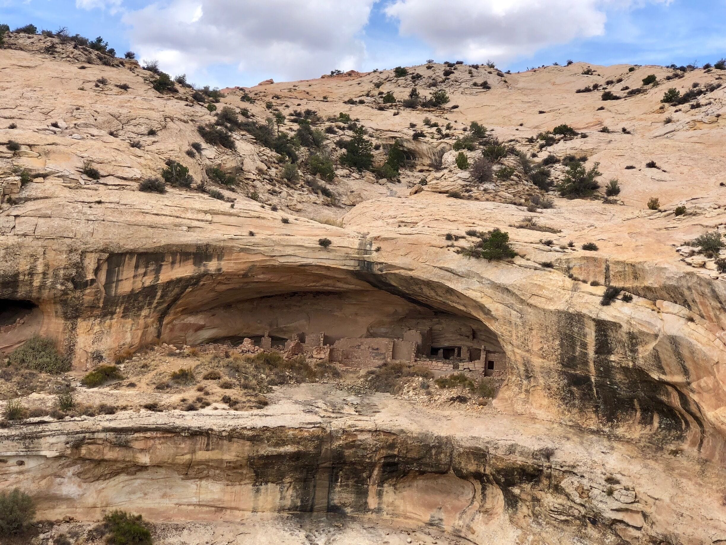 A large rock formation with an archway and ancient ruins at its base.