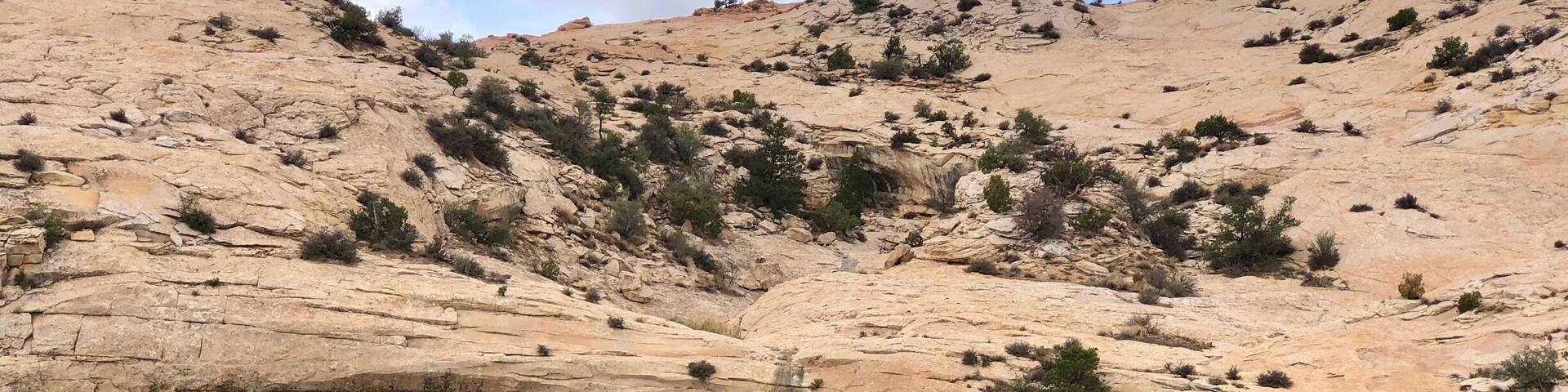 Una gran formación rocosa con un arco y ruinas antiguas a su base.