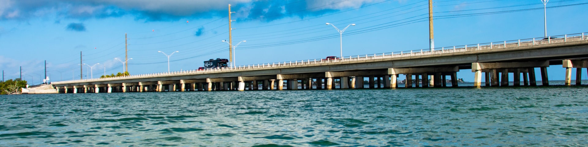 A bridge over water with streetlights and a cloudy sky.