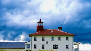 A white building with a red roof and a lighthouse tower, surrounded by tall grass and under a cloudy sky.