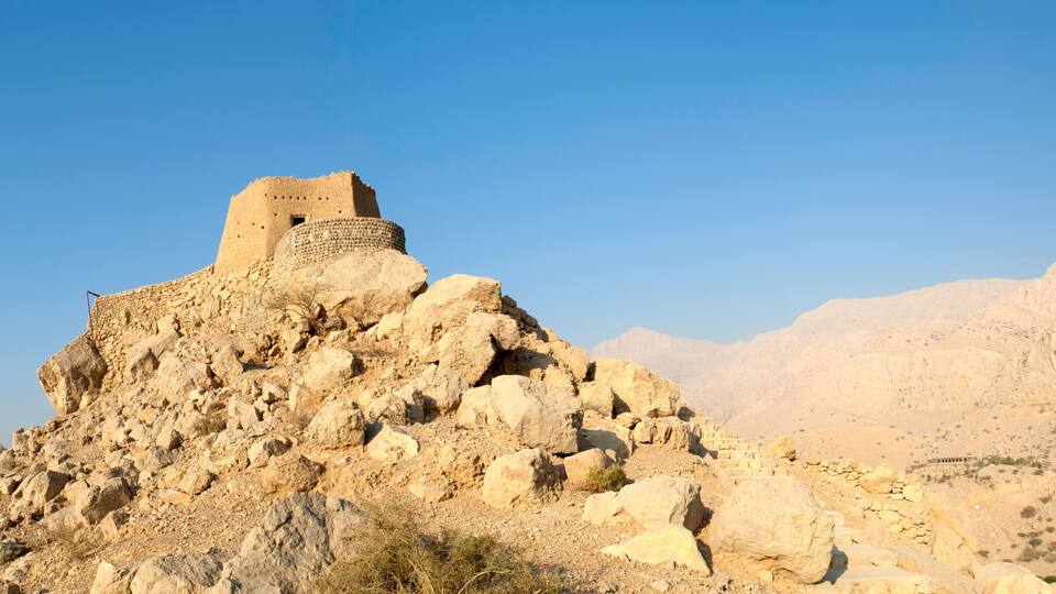 A rocky hill with a stone structure on top, surrounded by desert landscape.