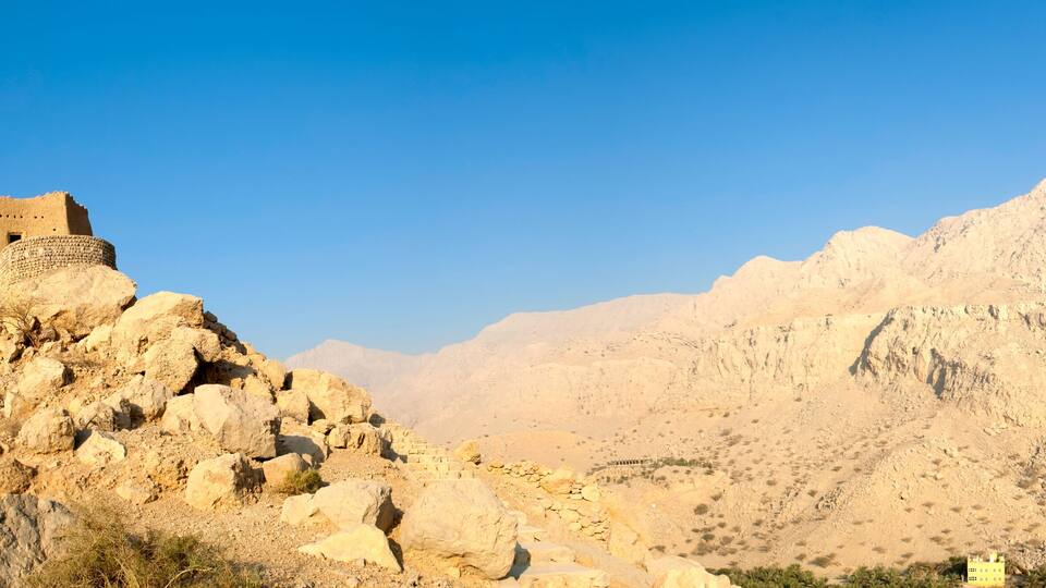 A rocky mountain with a small fortification on top and a large, barren hill in the background.