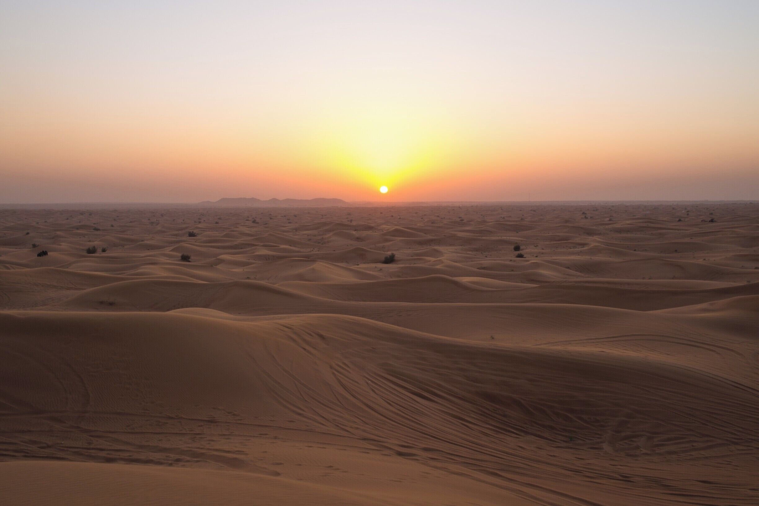 A desert landscape with sand dunes and a setting sun.
