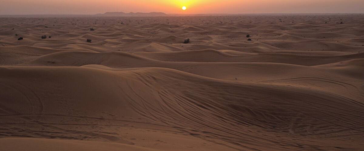 A desert landscape with sand dunes and a setting sun.