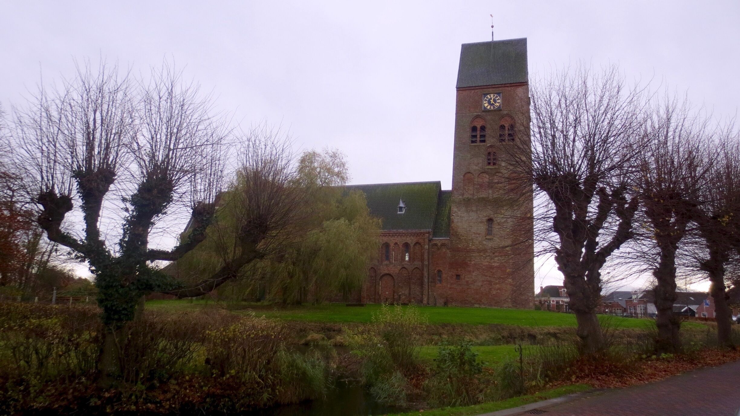 A historic building with a clock tower, surrounded by trees and a small pond.